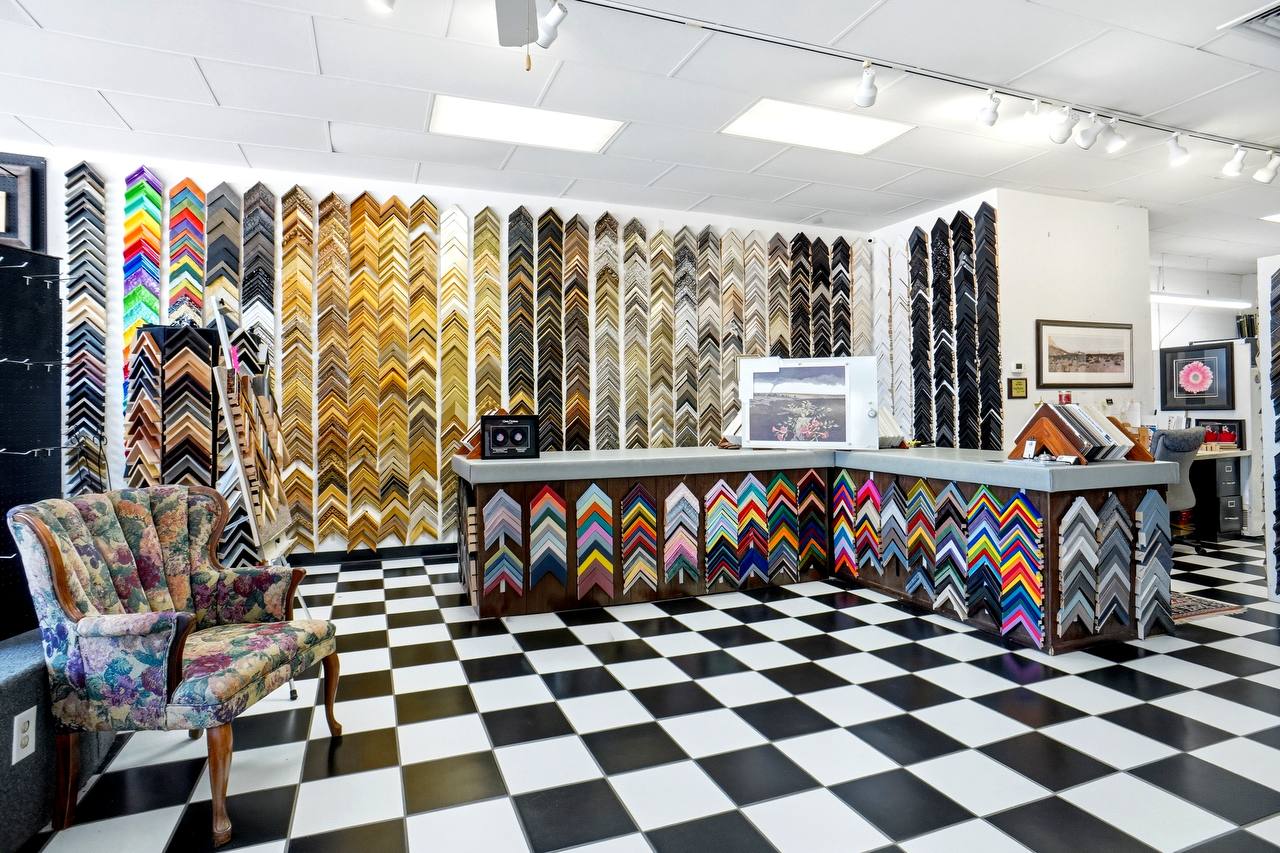 Inside The Frame Up: the front counter backed by a full wall of colorful moulding corner samples, the signature black-and-white checkerboard floor, and a vintage armchair