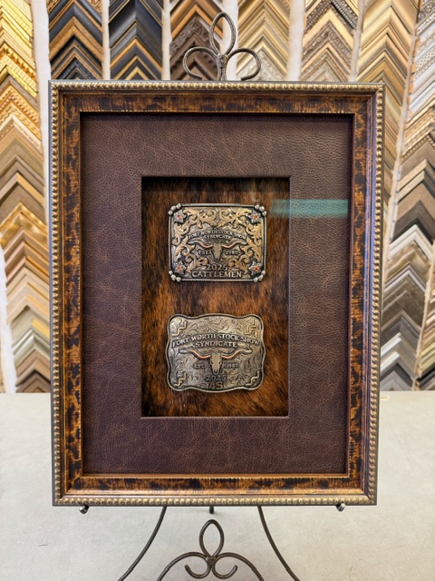 Fort Worth Stock Show belt buckles displayed on cowhide in a rustic shadowbox
